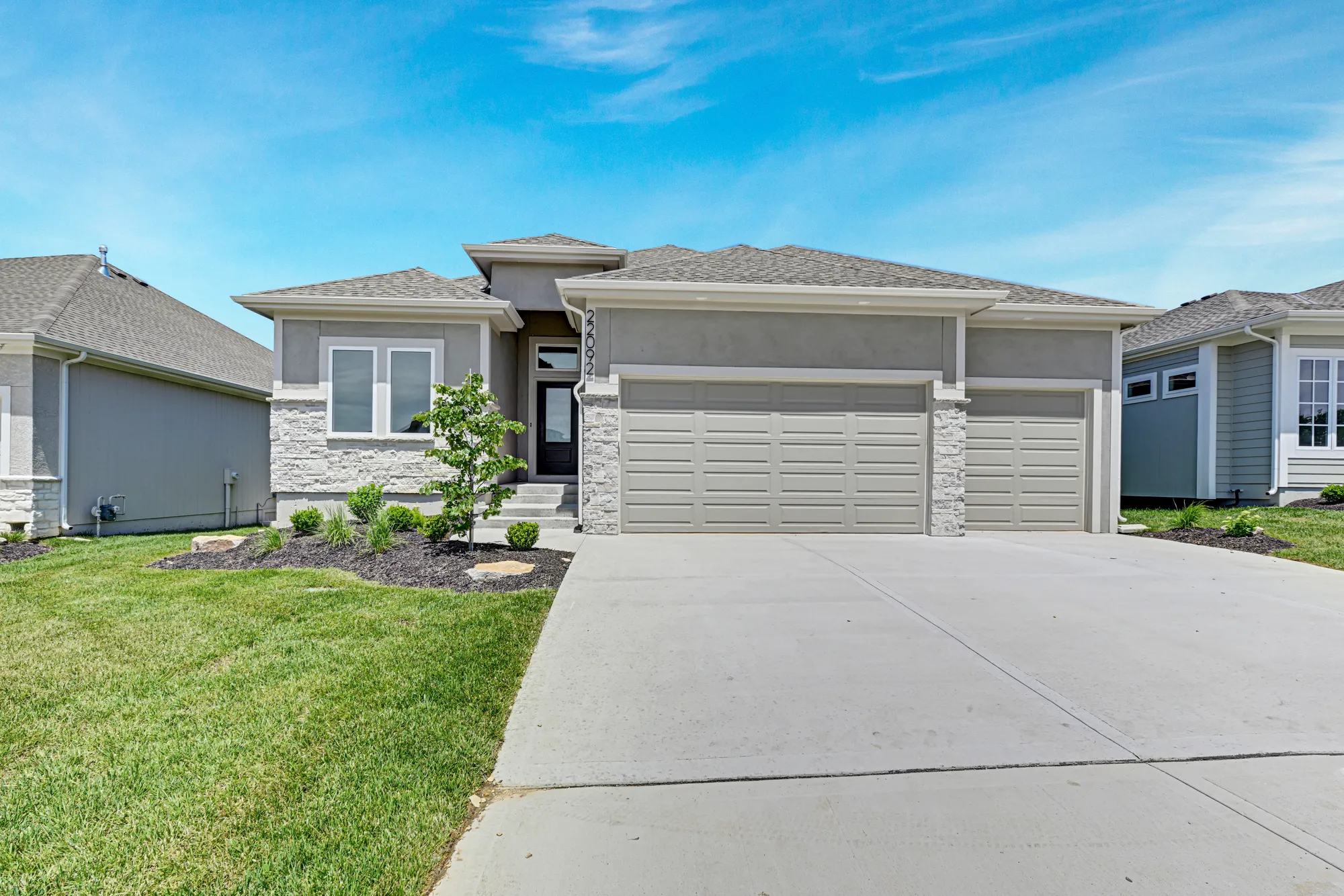 Front view of a modern gray suburban house with a two-car garage and small landscaped yard under a clear blue sky.