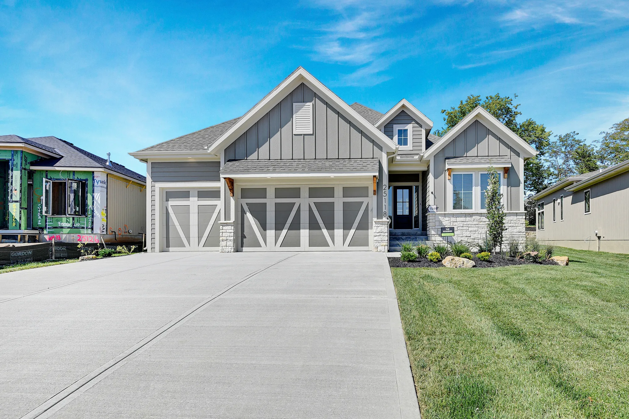 Newly built gray two-story house with white trim and a two-car garage; blue sky above.