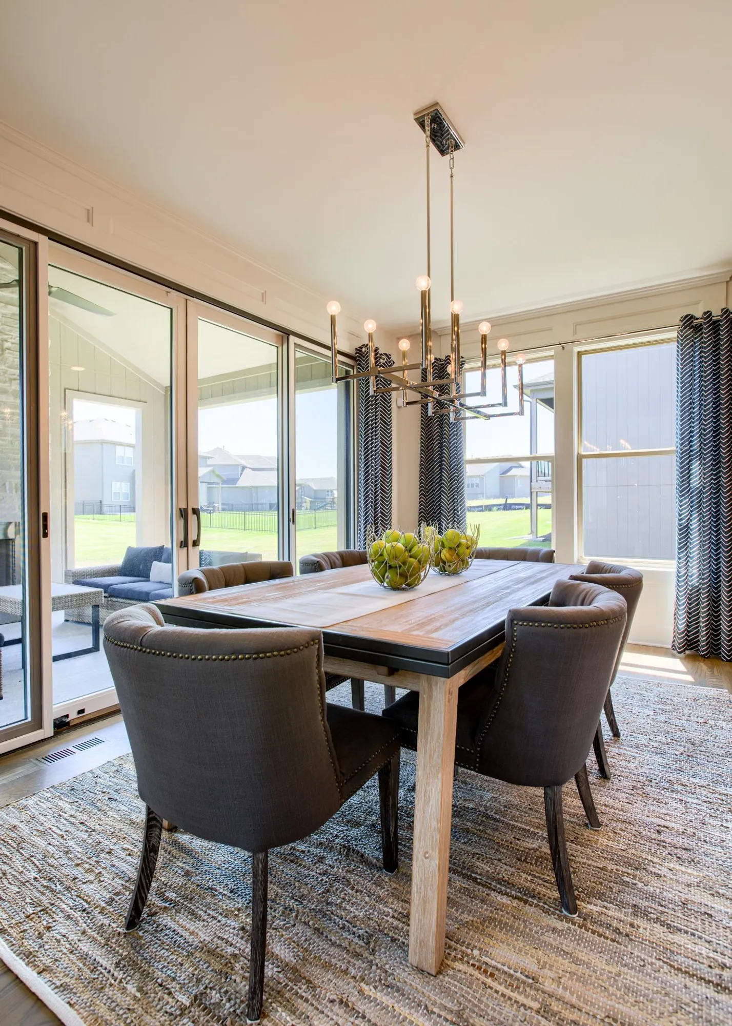 Modern dining room with a wooden table and dark upholstered chairs beneath a brass chandelier.