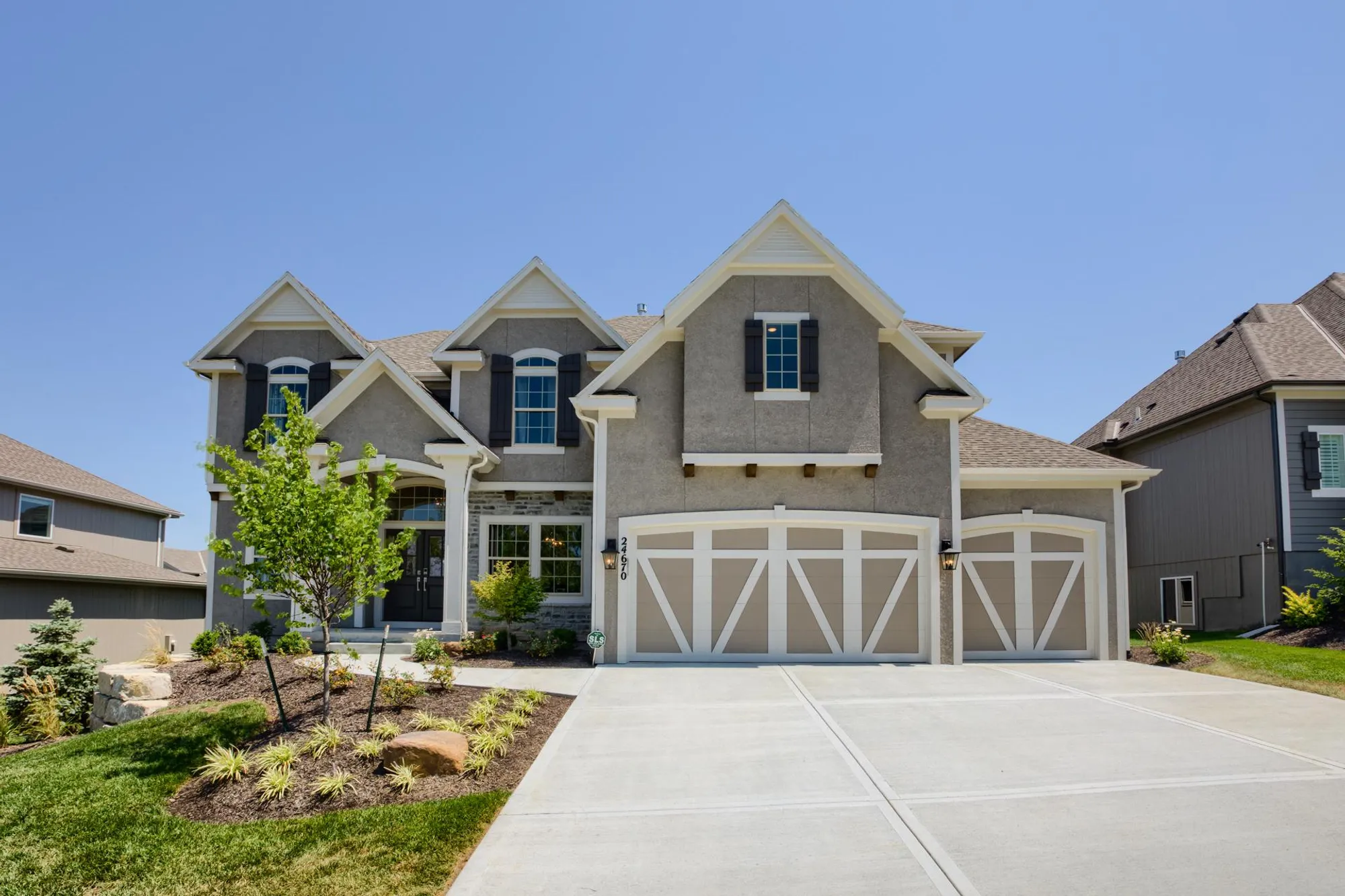 Modern two-story gray suburban house with a two-car garage and a manicured front yard under a clear blue sky.