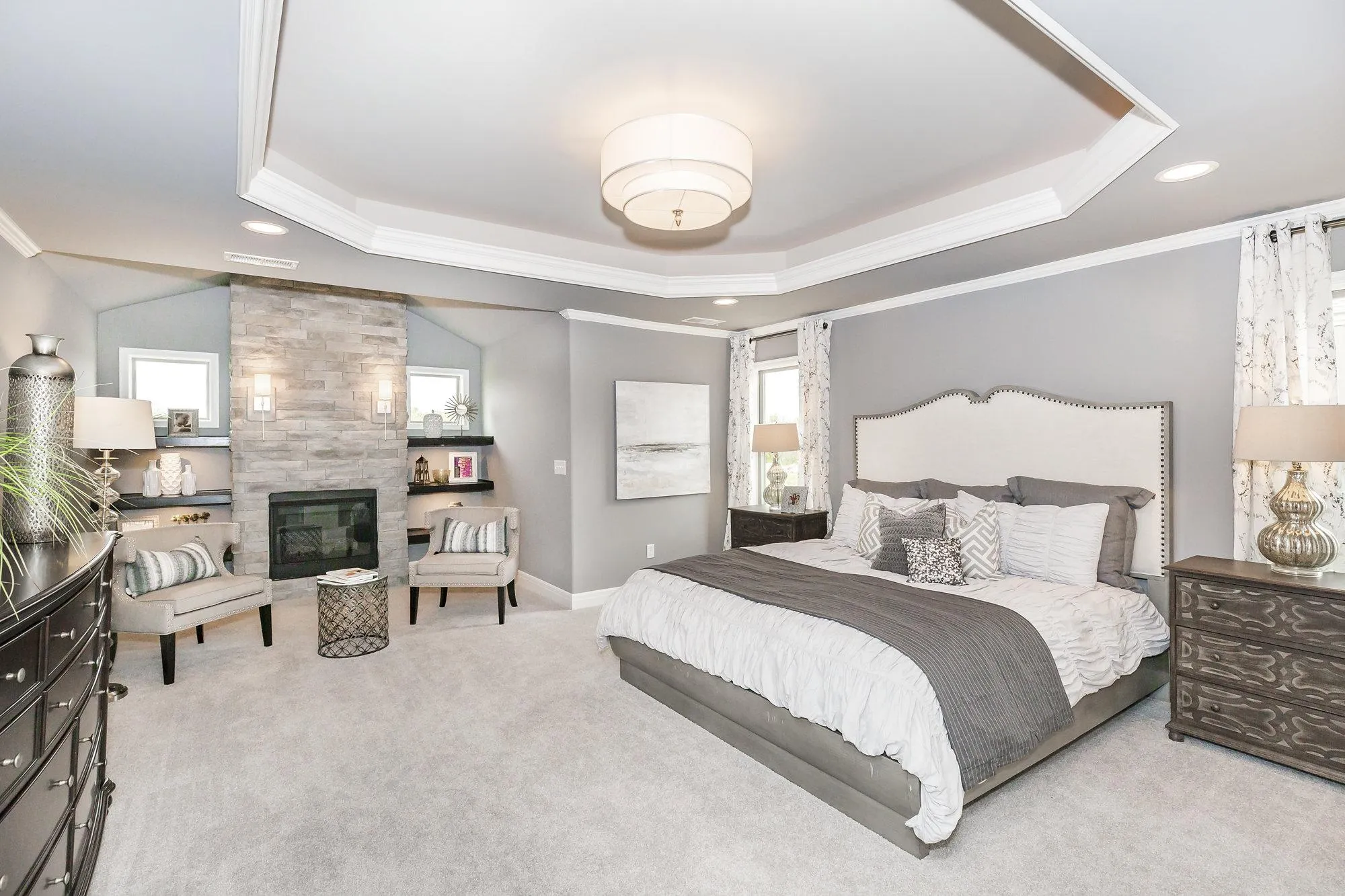 Luxurious gray-toned master bedroom with two tufted beds, matching nightstands, and a stone fireplace.