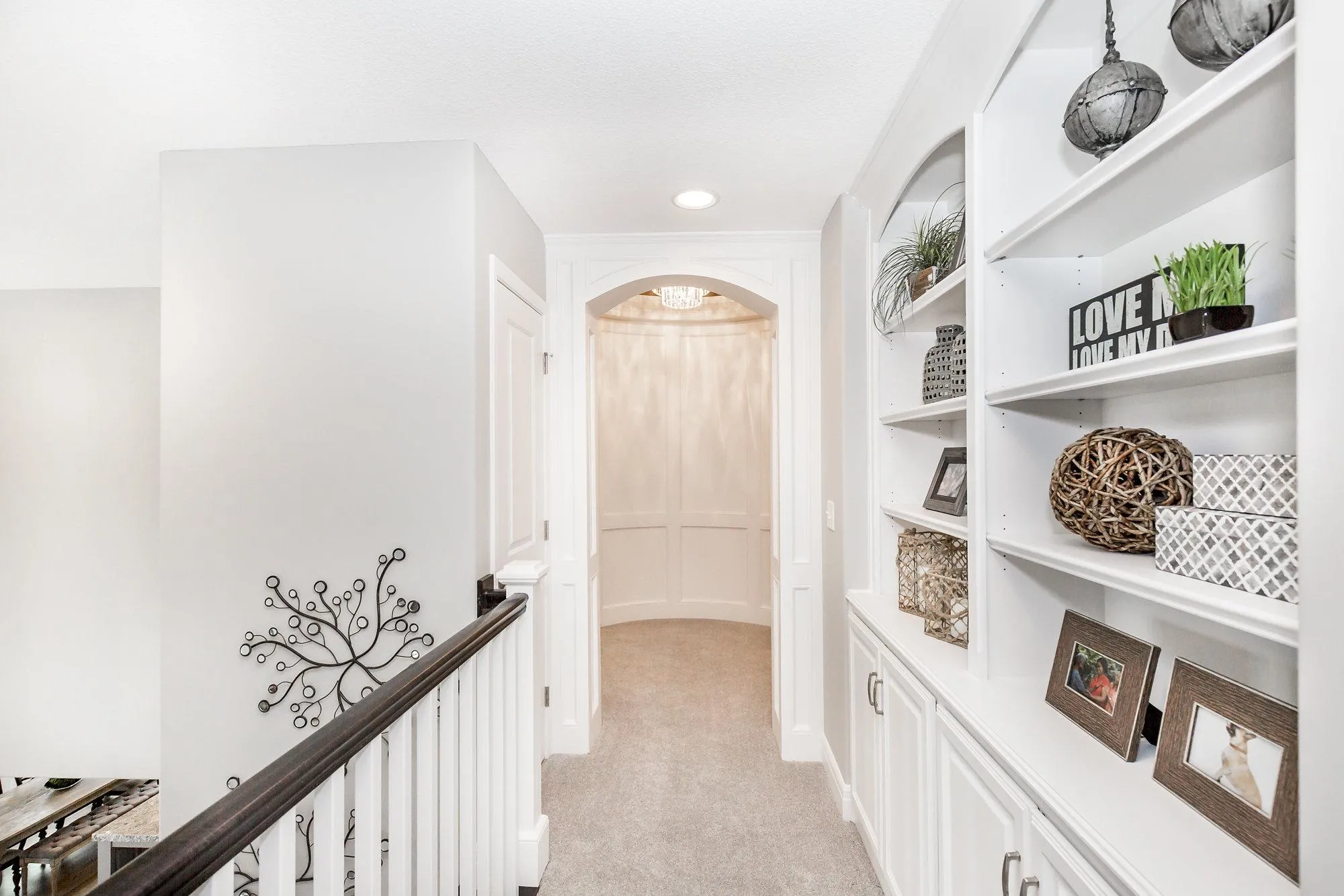 Bright white hallway with built-in shelves on the right displaying plants, baskets, and framed photos.