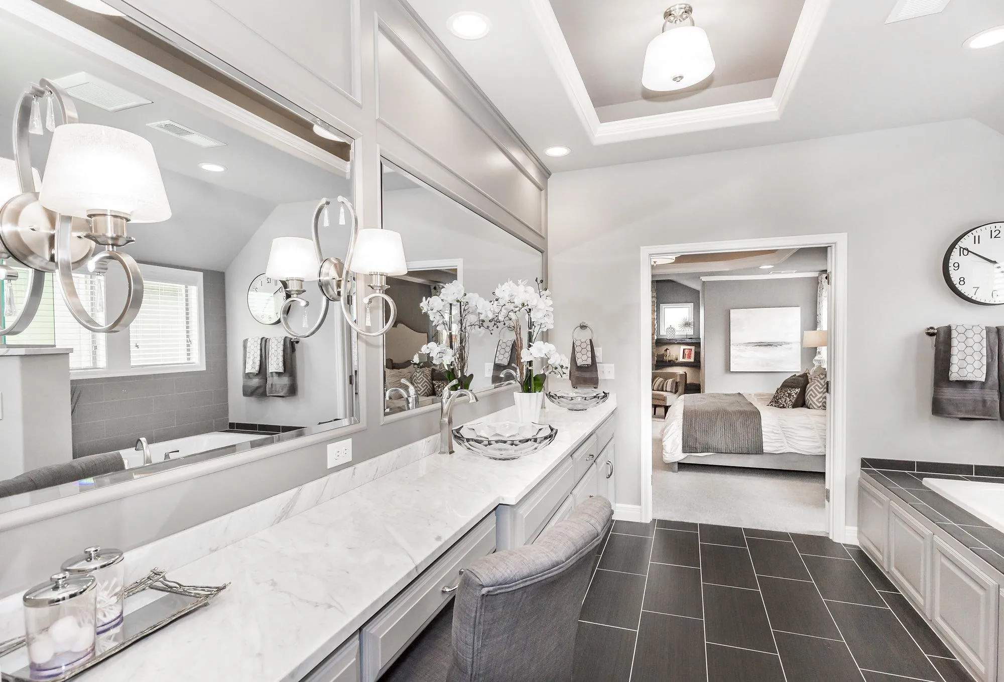 Bright modern bathroom with marble countertop, double sinks, and large mirrored cabinets, opening to a bedroom in the distance.