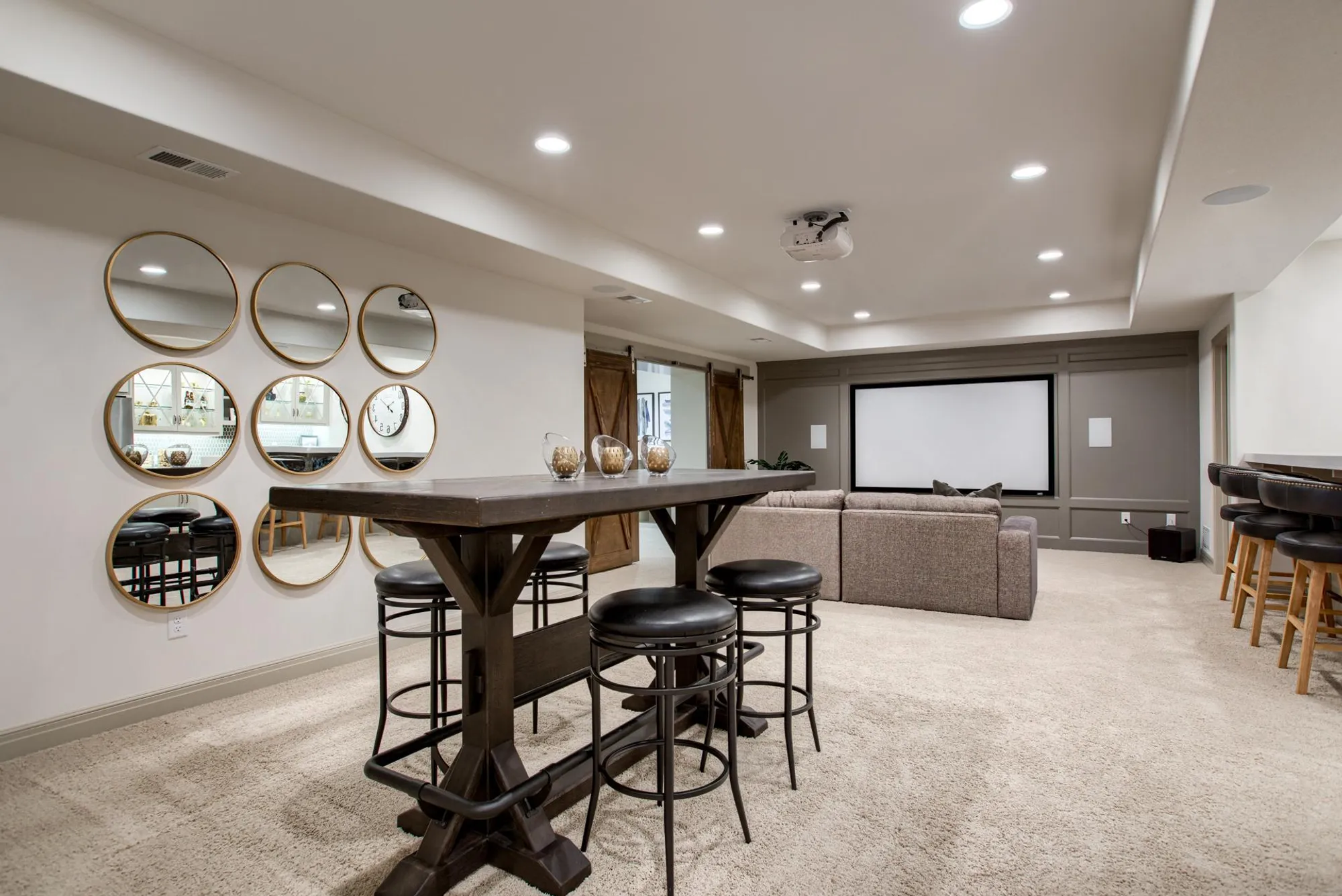 Basement lounge with a row of gold-framed circular mirrors, a long dark wooden table, and black bar stools.