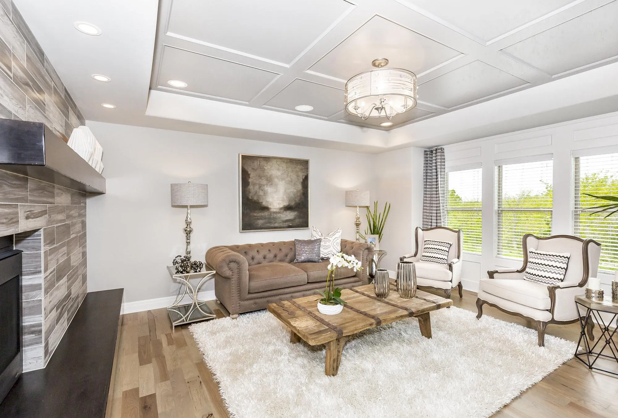Bright, modern living room with a tufted brown sofa, white armchairs, rustic wood coffee table, and a large shag rug underfoot.