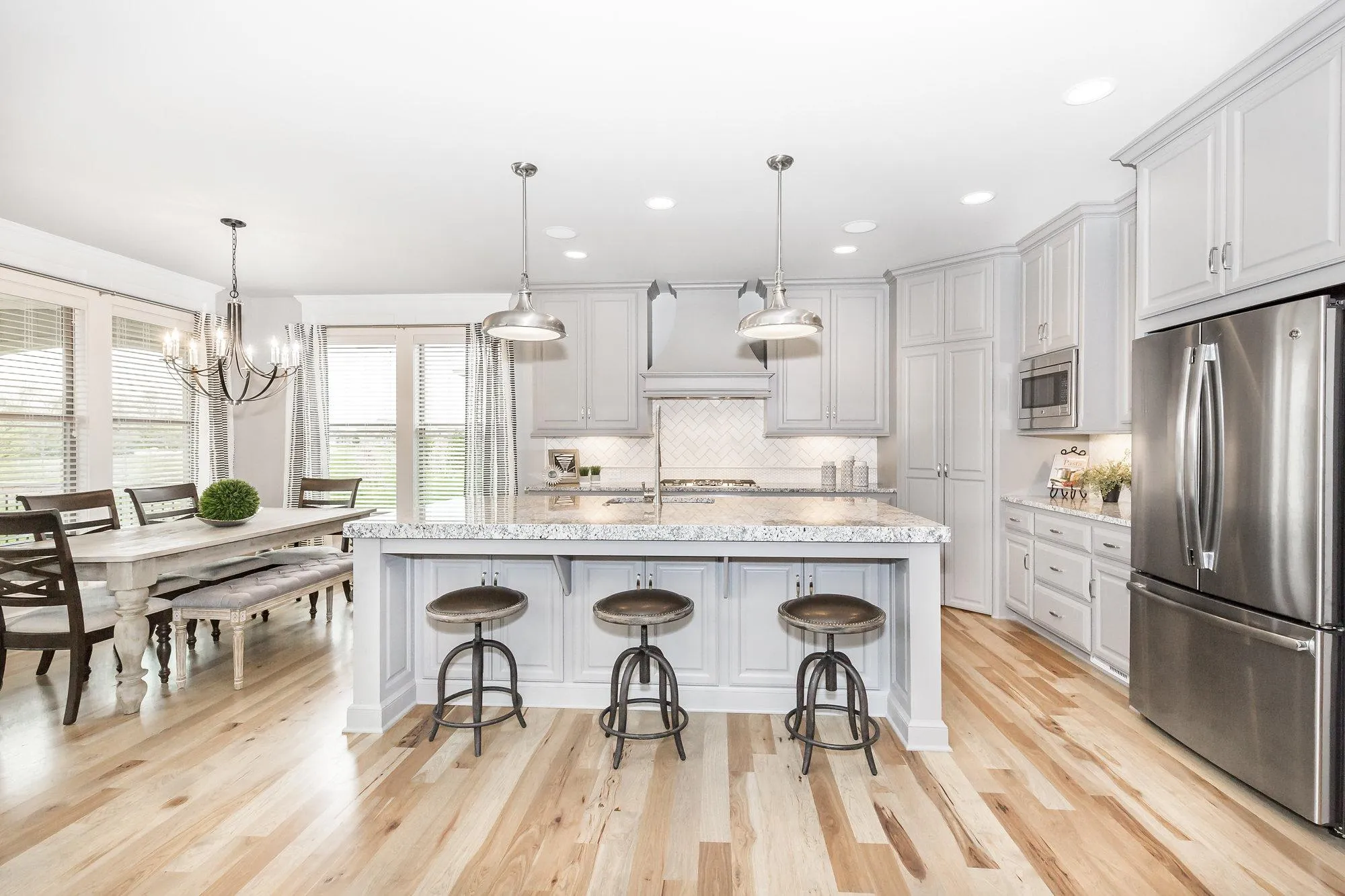 Bright white kitchen with marble island, pendant lights, and stainless-steel appliances including a large fridge.