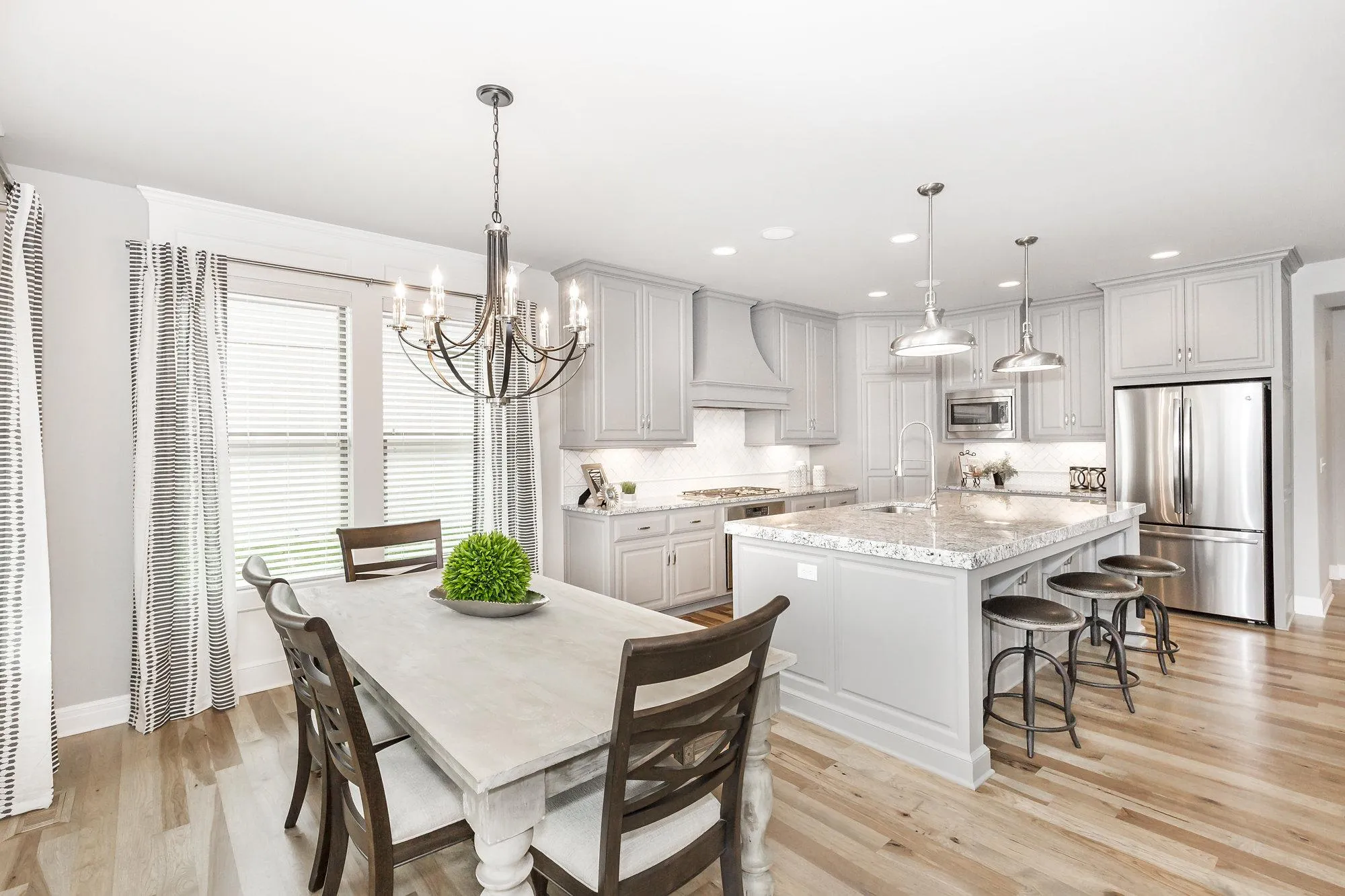 Bright, modern kitchen with gray cabinets, marble island, and stainless steel appliances; chandelier over dining table and pendant lights above the island.