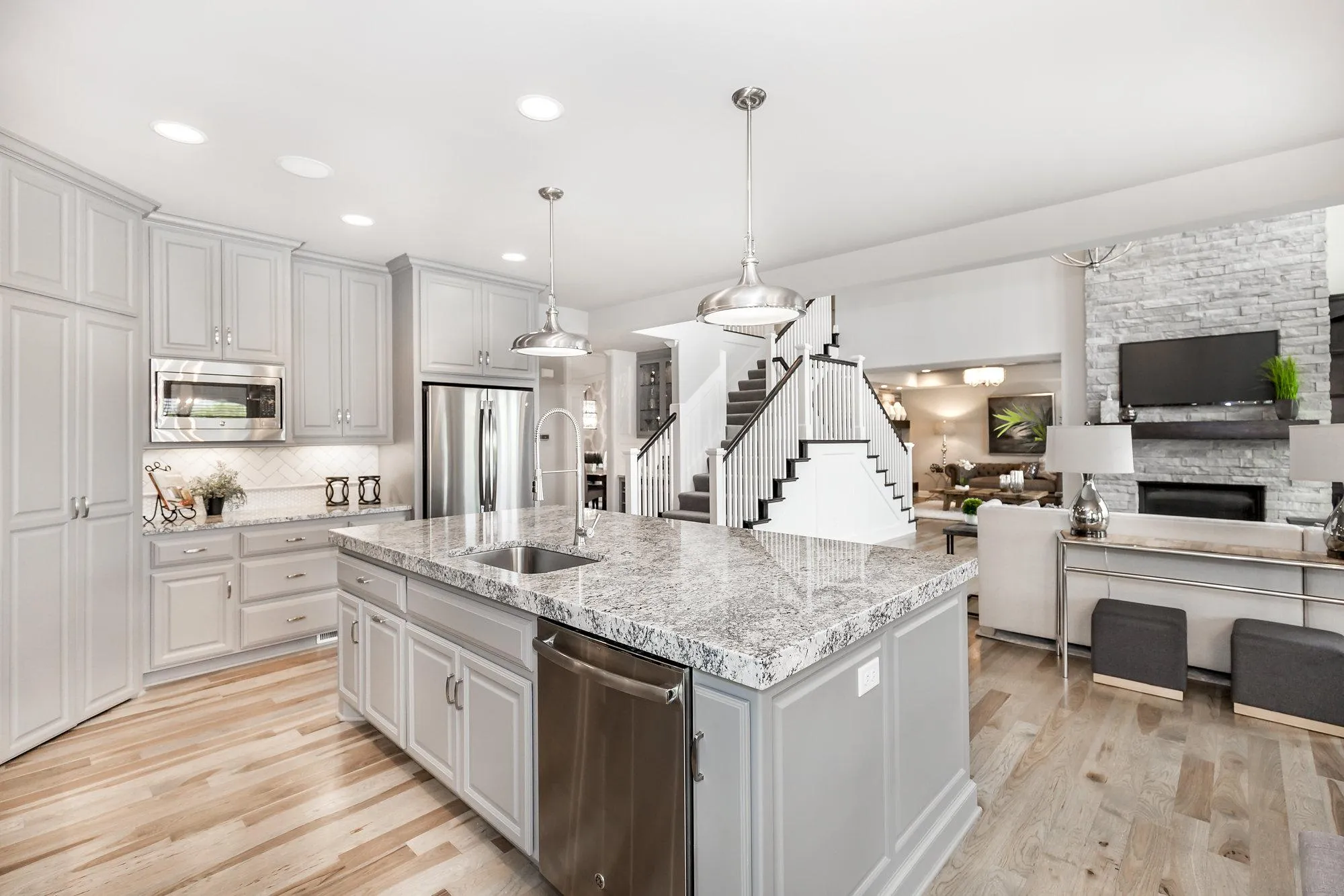Bright open-concept kitchen with gray cabinets, granite island, and stainless steel appliances under recessed lighting