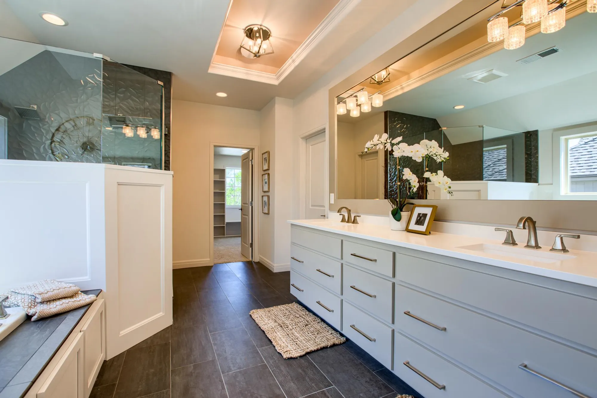 Contemporary bathroom with a long double-sink vanity, light gray cabinets, and a large mirror reflecting glass shower and pendant lights.