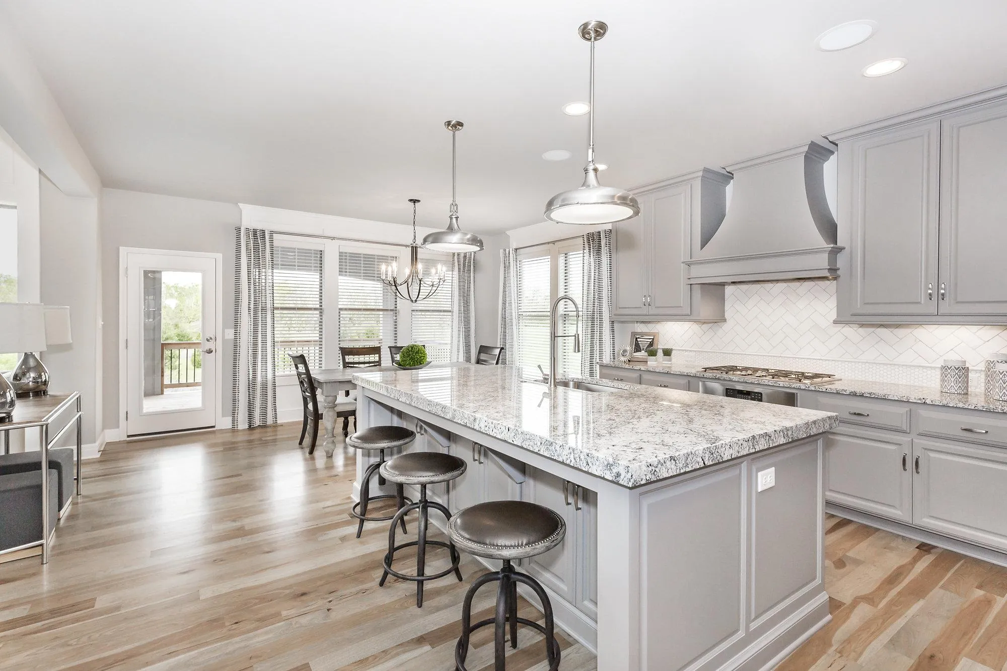 Bright modern kitchen with gray cabinets, granite island, and pendant lights over a spacious island.