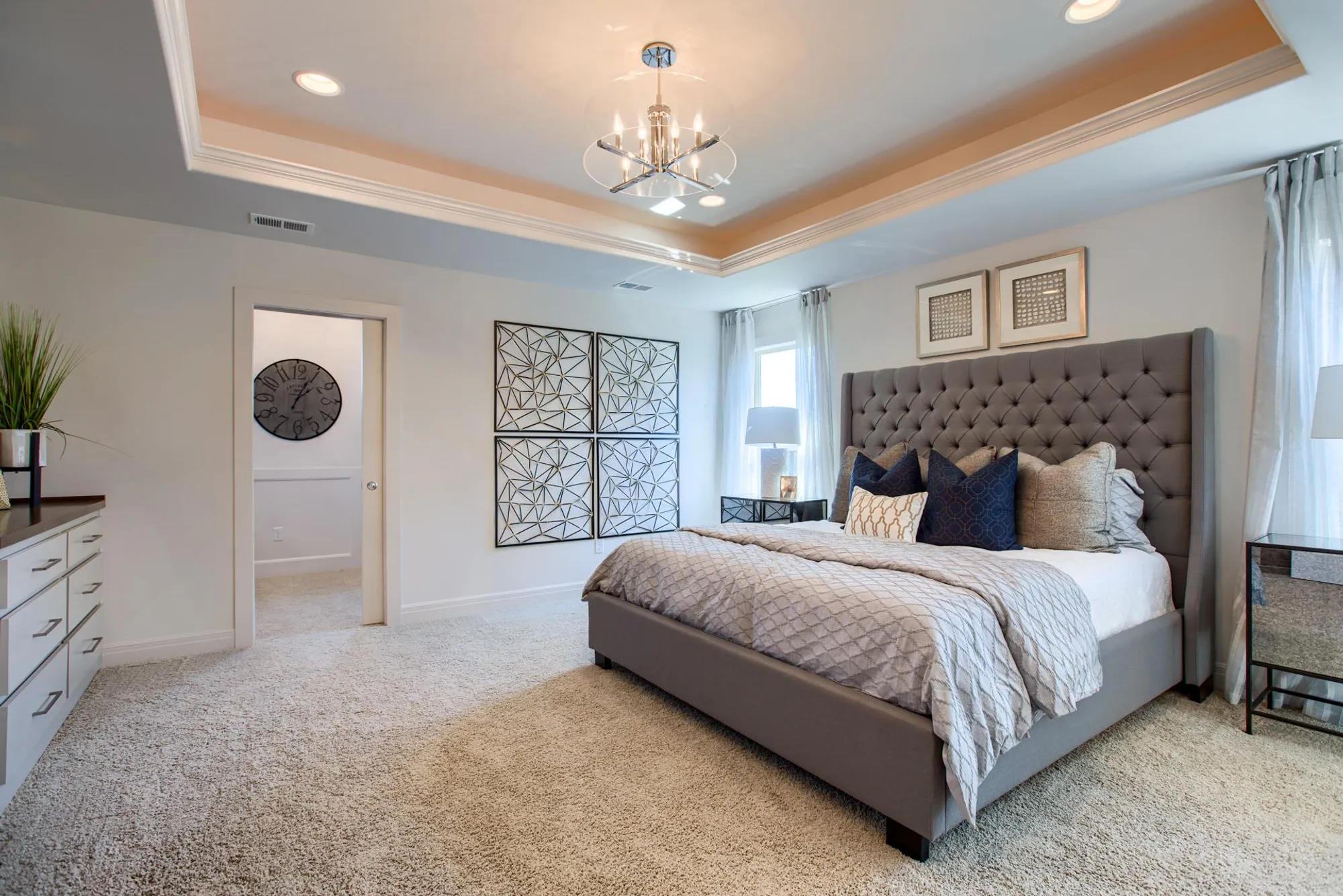 Luxurious gray upholstered bed with tufted headboard in a bright, contemporary bedroom with geometric wall art and neutral bedding.