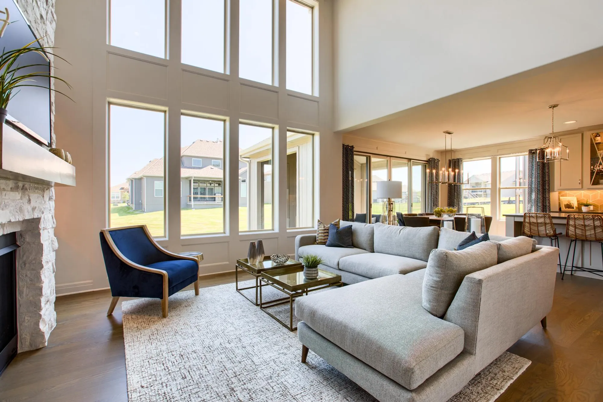 Open living room with tall grid windows, light gray sectional sofa, blue accent chair, and glass coffee table.
