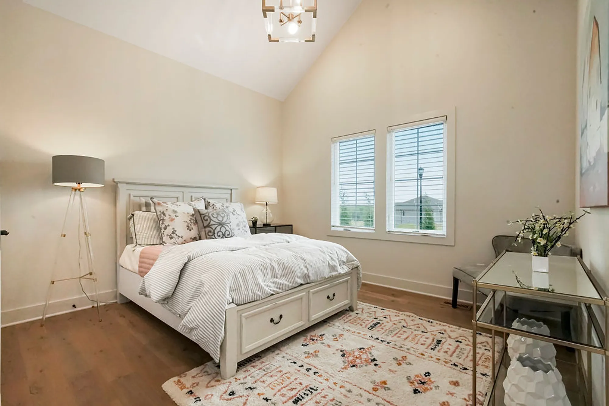 Bright, modern bedroom with a white bed, headboard, matching nightstands, and decorative pillows under natural light from two windows in the corner room.