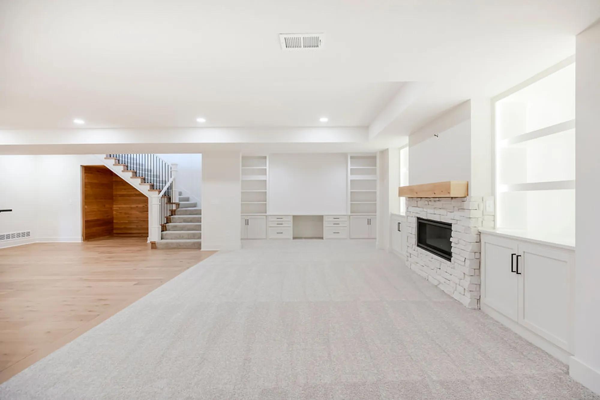 Bright open living area with white built-in cabinetry, a stone fireplace, and a wooden staircase on the left.