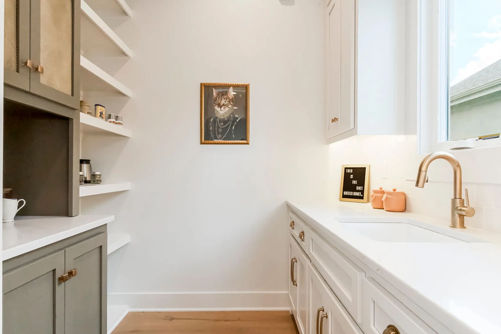 Bright kitchen with white cabinets, open shelves, and a framed cat portrait on the wall near the sink area.