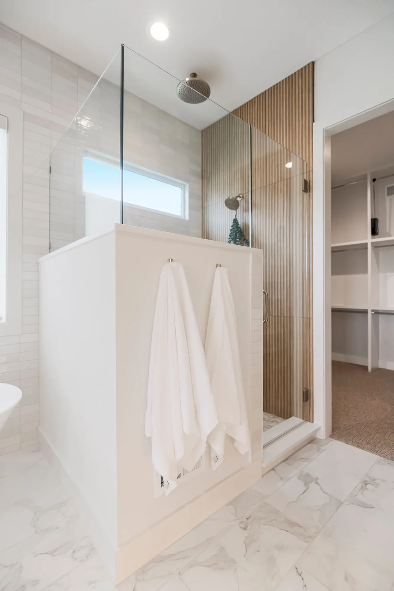 Modern bathroom with a glass shower enclosure, marble floor, and a wood-paneled wall; two white towels hang on a built-in partition.