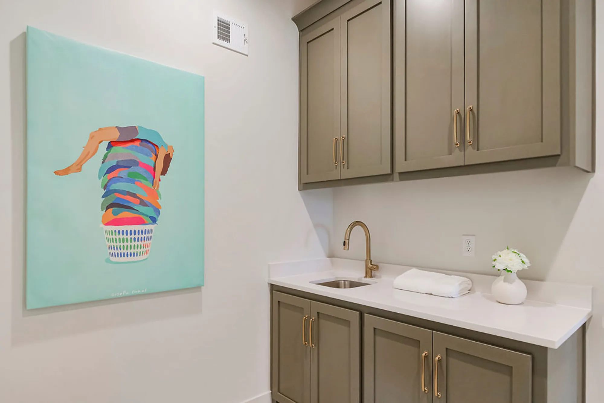 Modern laundry room with gray cabinets, white countertop, and a colorful wall art piece featuring a stacked laundry basket on the left.