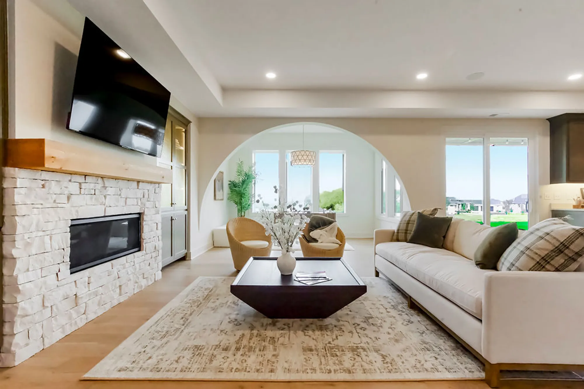 Bright living room with a white sectional sofa, stone fireplace, and wall-mounted flat-screen TV above the mantel.