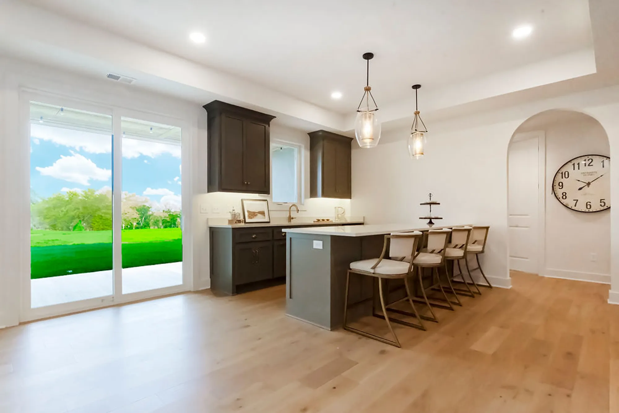 Open-concept kitchen with a dark island, bar seating, pendant lights, and sliding glass doors to a sunny backyard.