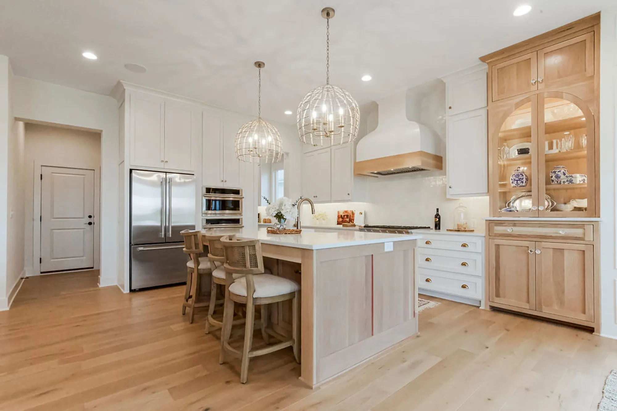 Bright kitchen with white cabinets, a light wood island, and wicker bar stools under two spherical cage pendant lights.