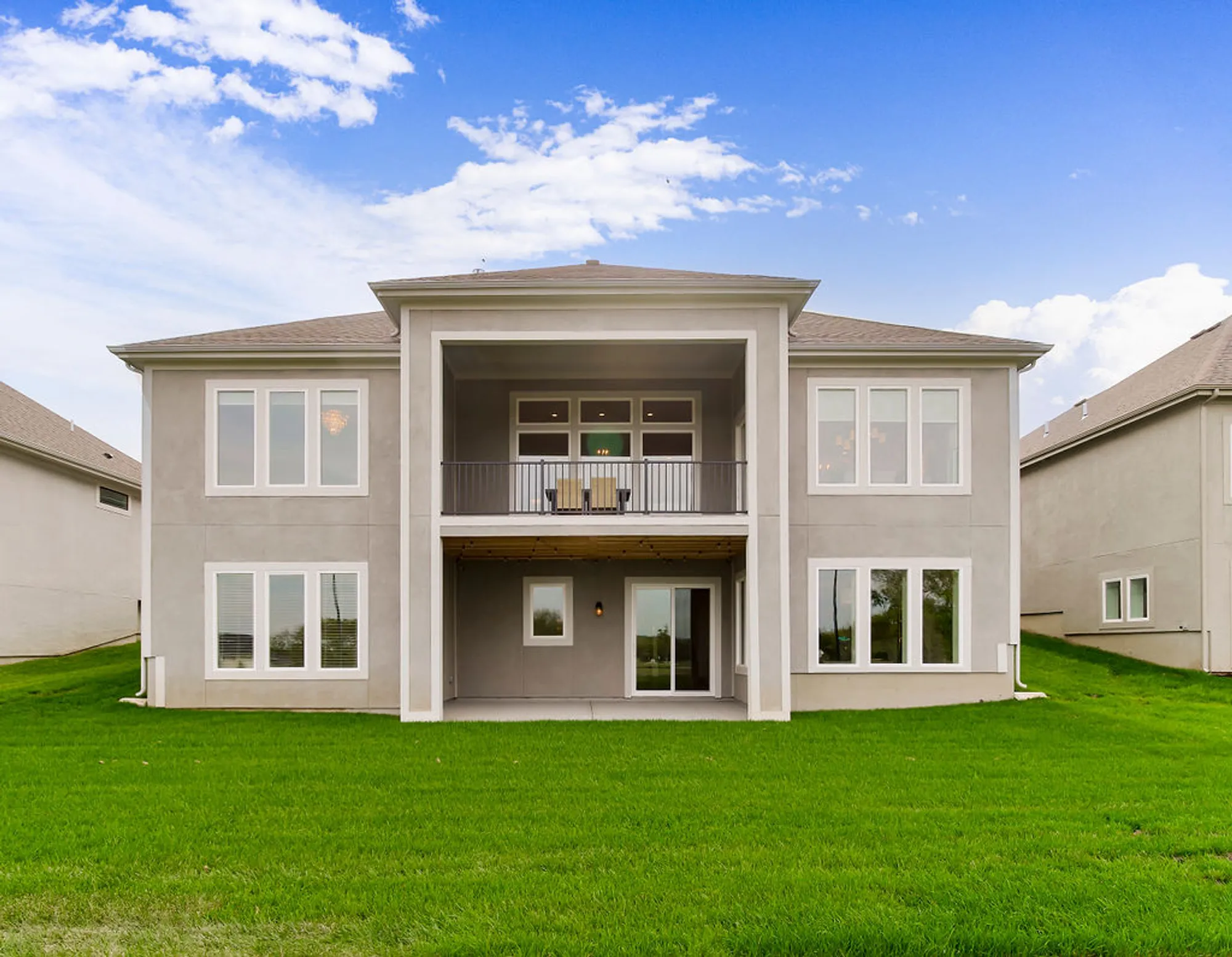 Modern gray townhouse with a central balcony, large windows, and green lawn under a blue sky.