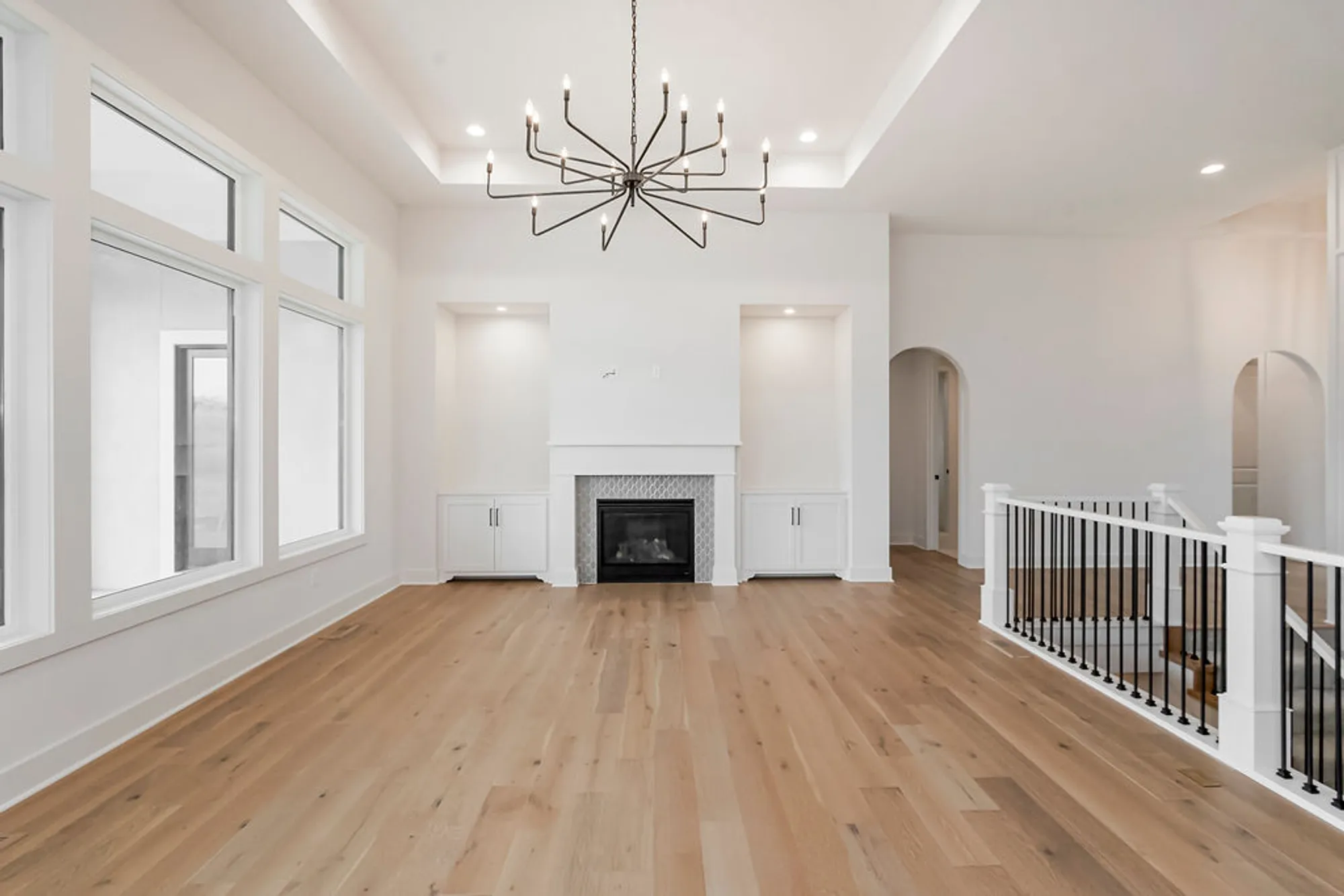 Bright open living room with white walls, large windows, and a black metal chandelier over a white fireplace and built-in cabinets on either side.