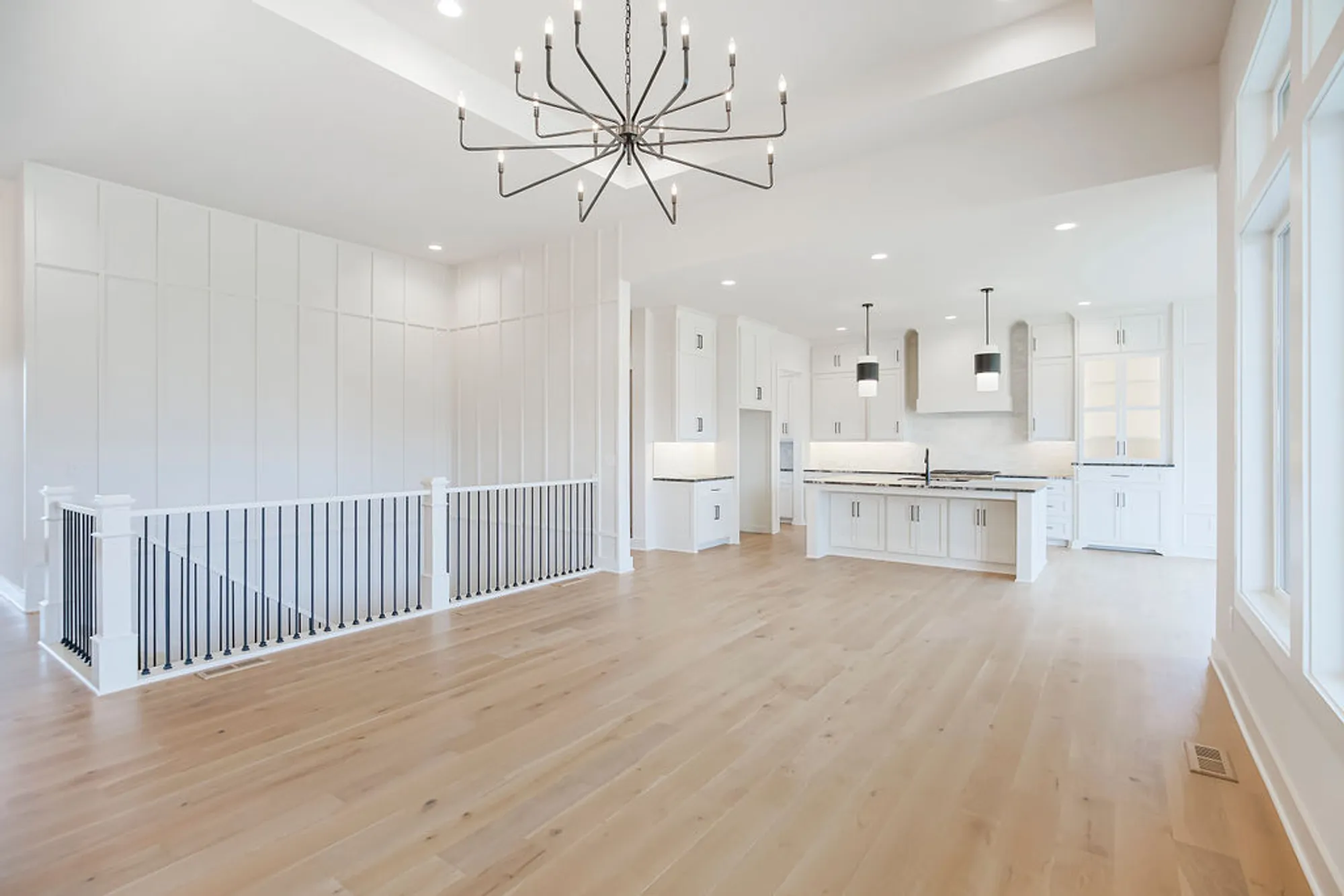 Bright open-concept kitchen with white cabinets, light wood floors, and a geometric chandelier hanging from the ceiling.