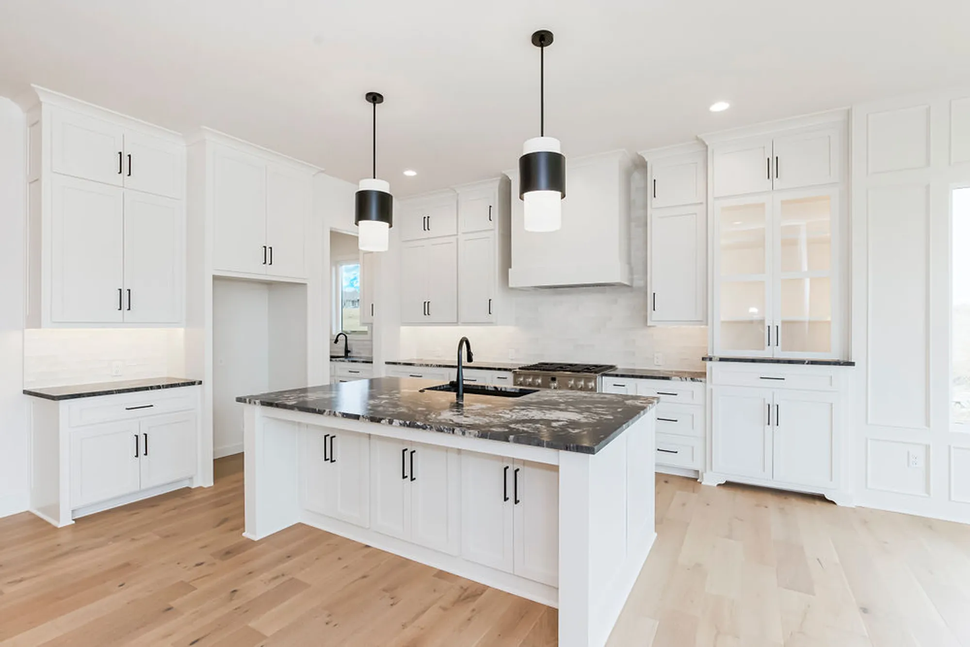 Bright white kitchen with shaker cabinets, black hardware, and a marble-topped island under two pendant lights