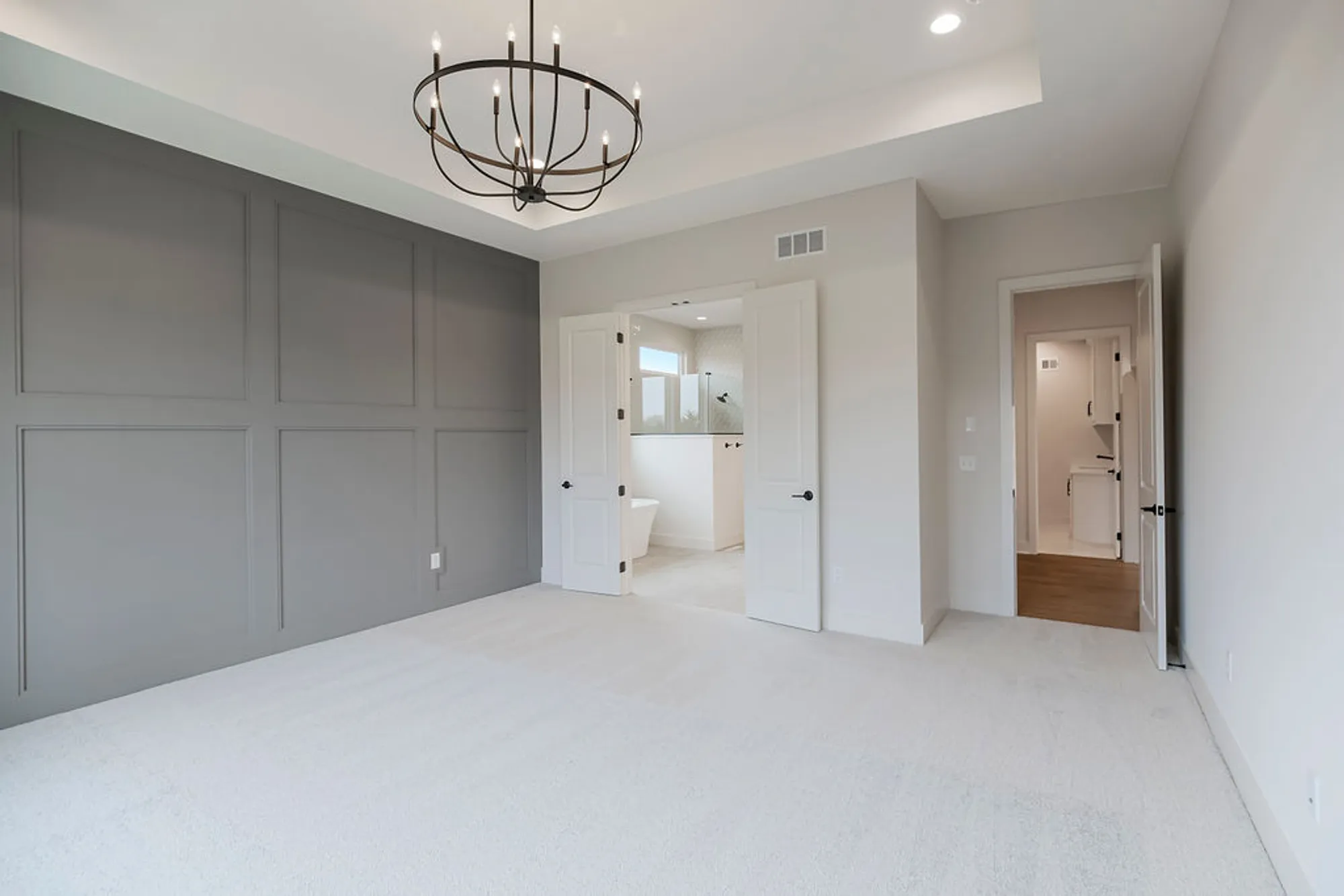 Empty modern bedroom with a gray paneled accent wall, white doors, and a circular metal chandelier above.