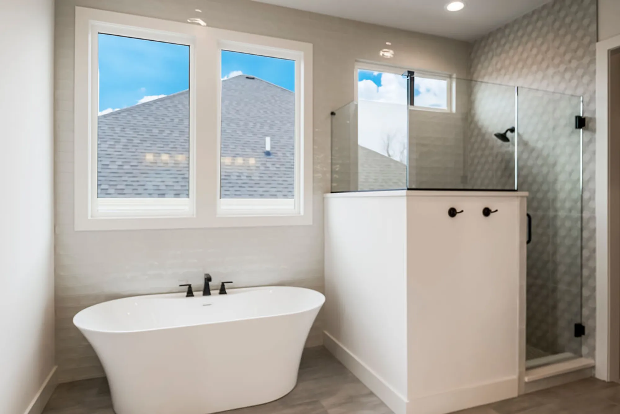 Modern bathroom with a white freestanding oval tub, two windows, and a glass-enclosed shower.