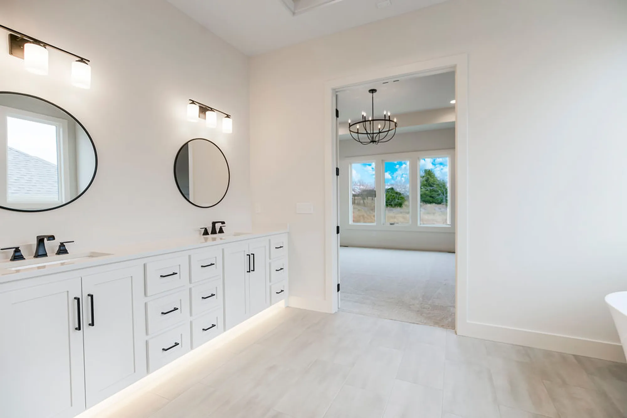 Bright bathroom with white cabinetry, two round mirrors, and black fixtures under warm sconces.