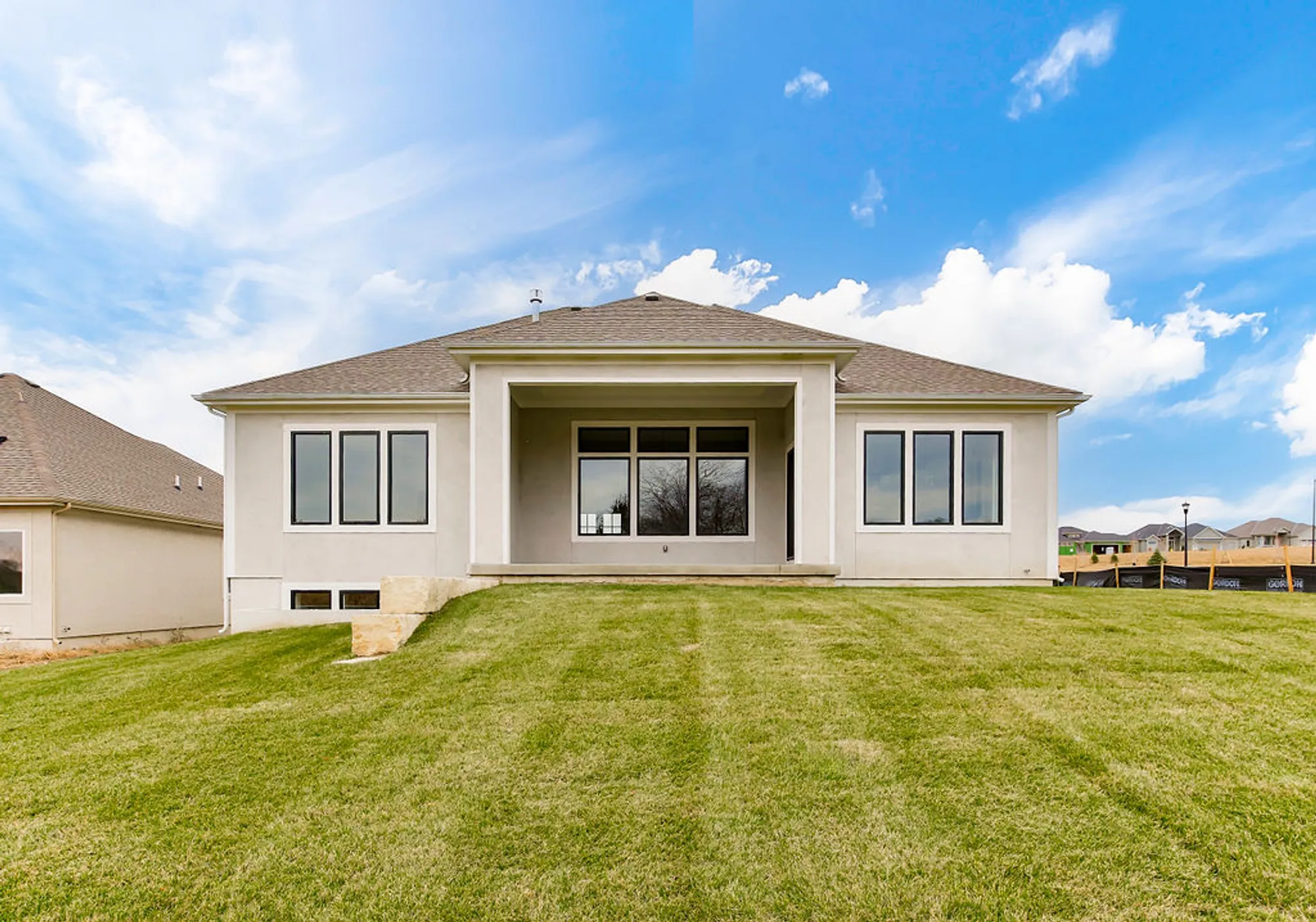 Front view of a modern two-story house with large windows and a covered entry, sitting on green lawn under a blue sky.