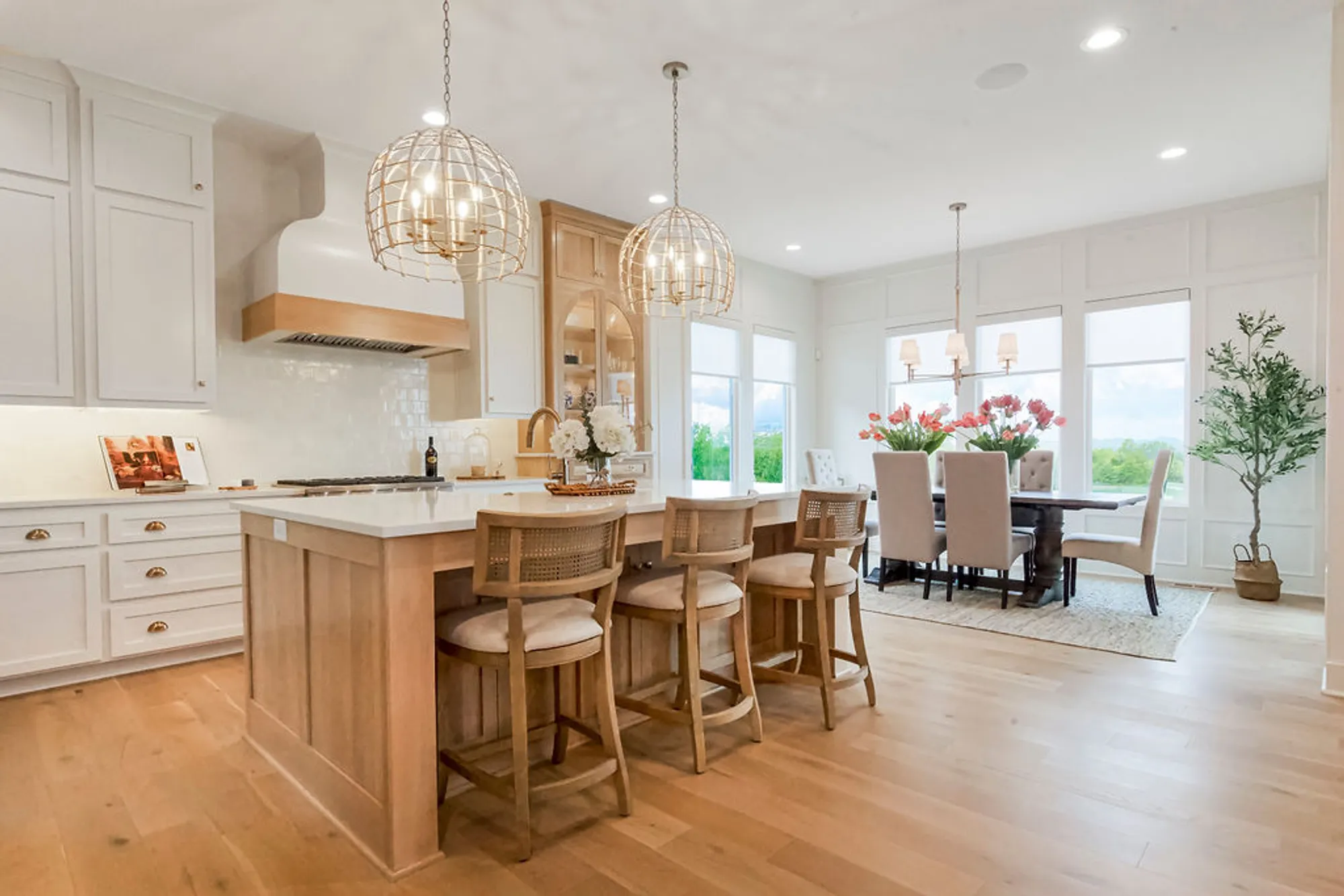 Open-concept kitchen and dining area with white cabinets, a wooden island, brass hardware, and two spherical wire pendant lights above the island.