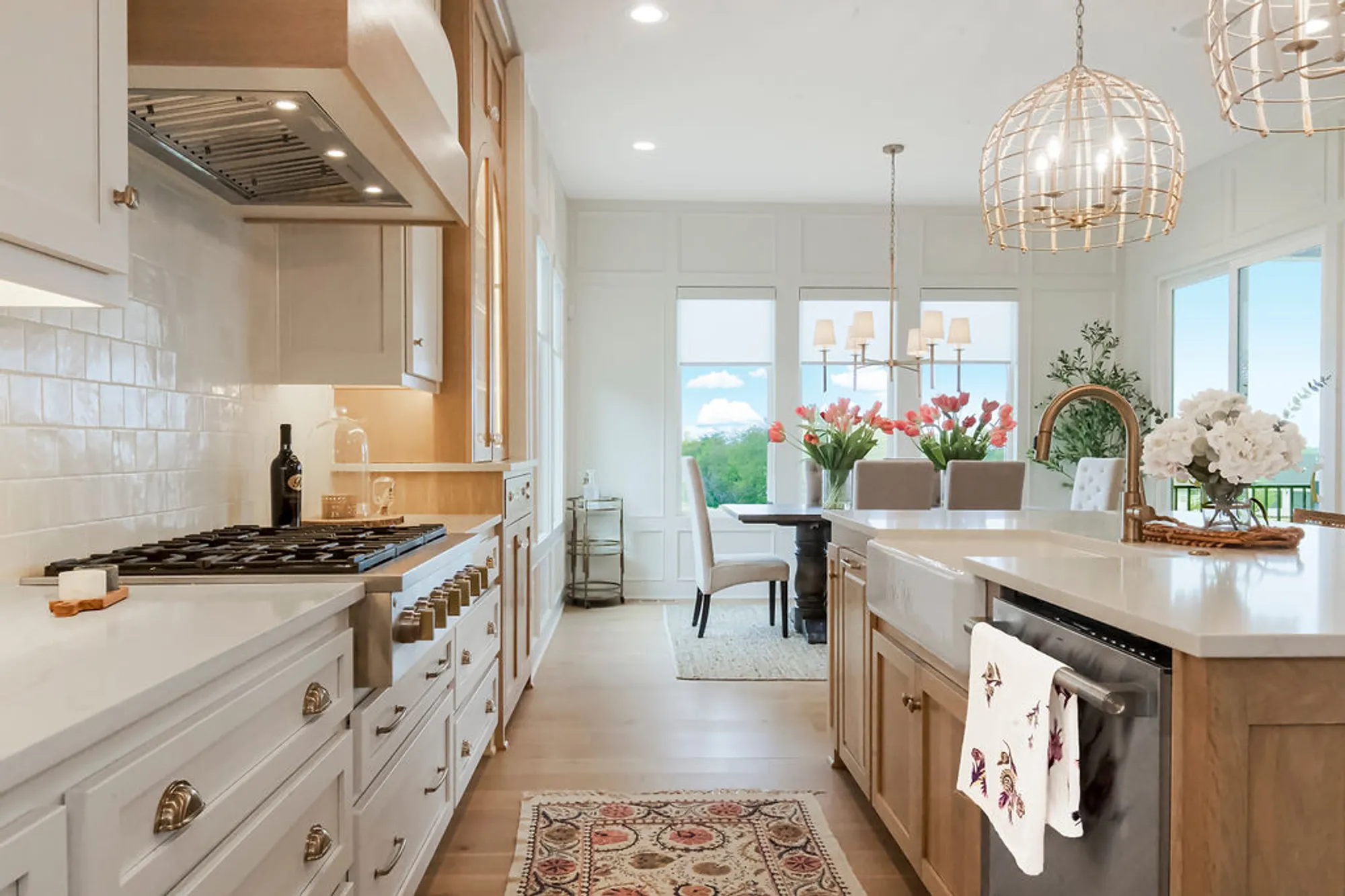 Bright modern kitchen with white cabinets, a gas range on the left, and a large island adorned with towels and flowers.