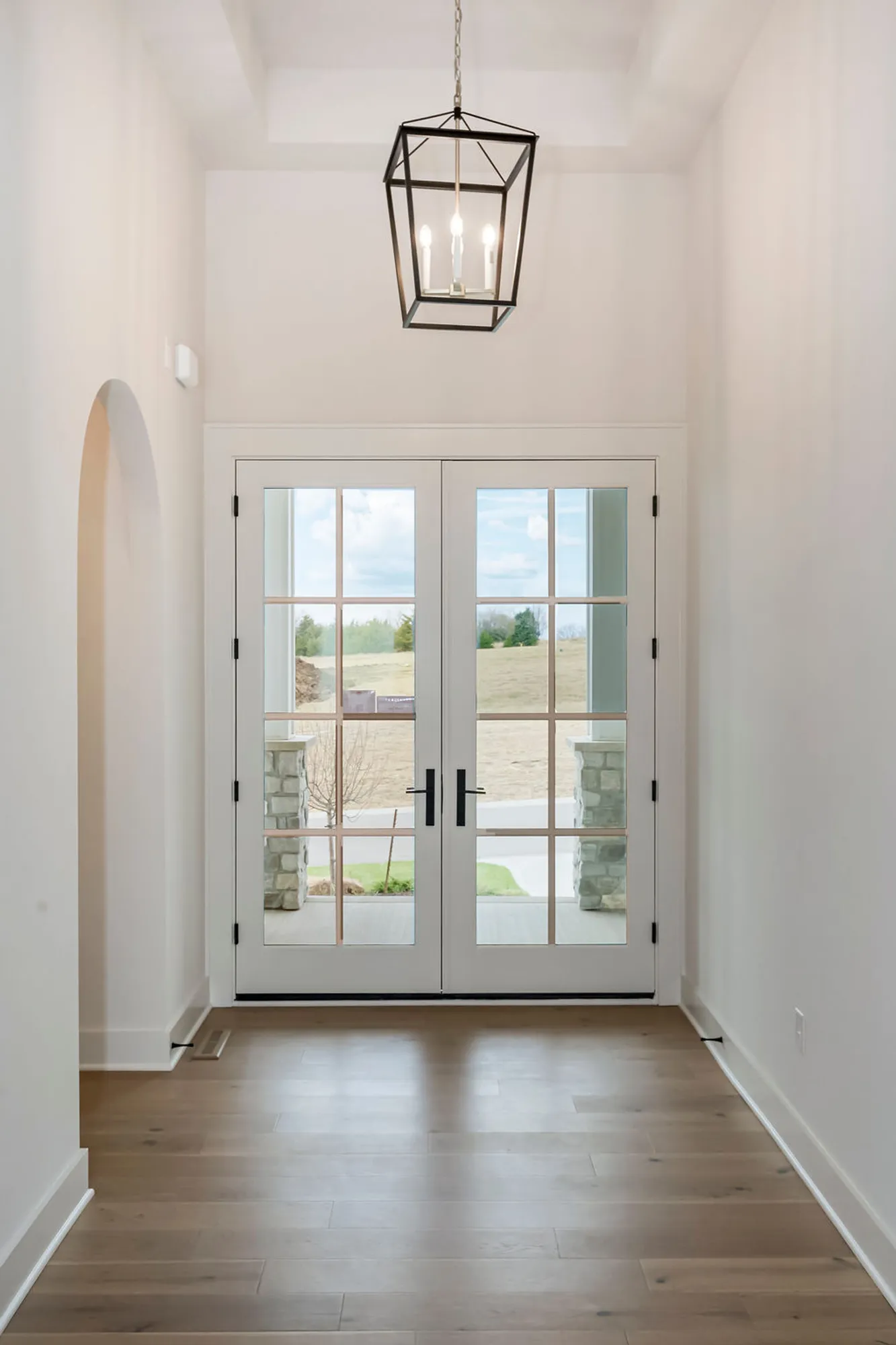 Bright entry hall with white walls, a geometric pendant chandelier, and glass French doors opening to outdoors.