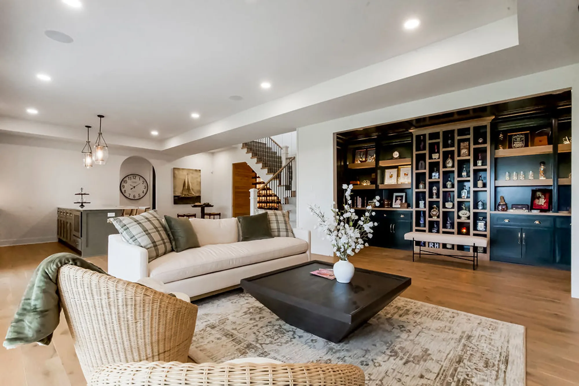Open-concept living room with a white sofa, plaid cushions, wicker chairs, and a dark rectangular coffee table facing a display wall of cabinets and shelves.