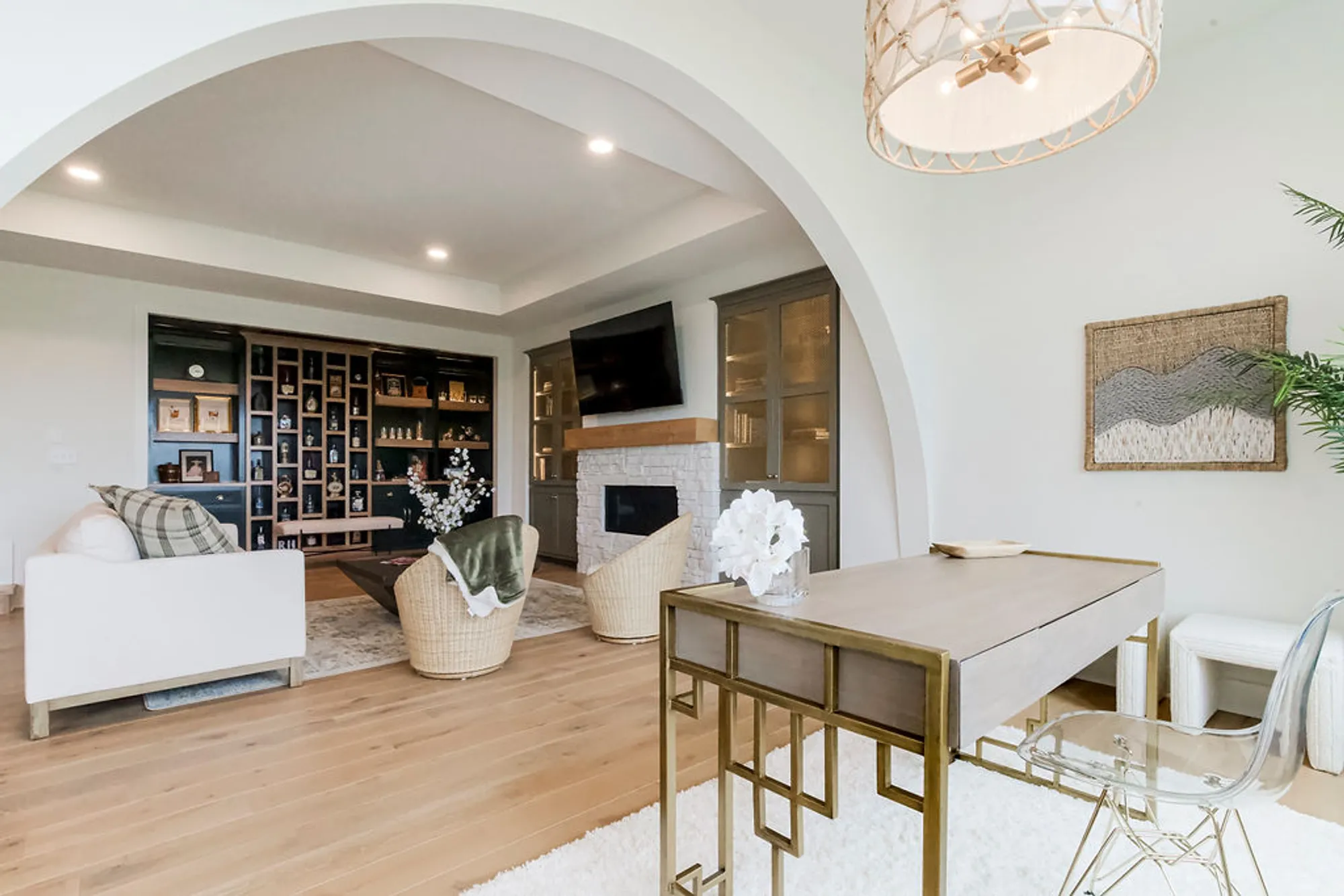 Open-concept living room with an arched doorway, dark wood shelving, and a wall-mounted TV above a light brick fireplace.